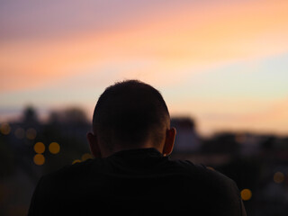 Jeune homme pensif de dos regardant au loin pendant un coucher de soleil.