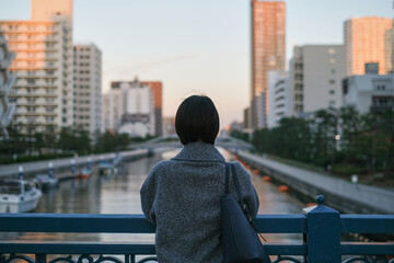 橋の上から夕暮れの街を眺める女性の後ろ姿