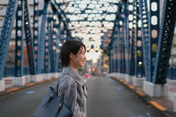 夕暮れの街の橋の上を歩く女性