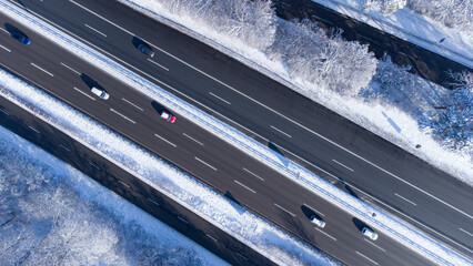Aerial top view of snow covered Autobahn highway in the south of Munich surrounded by forest in winter