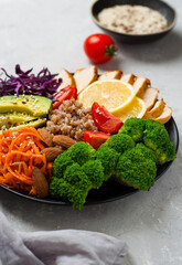 The concept of proper, nutritious nutrition, a bowl with chicken breast, buckwheat, vegetables, cabbage, broccoli, carrots, nuts, avacado and cherry tomatoes, On a light background, close up.