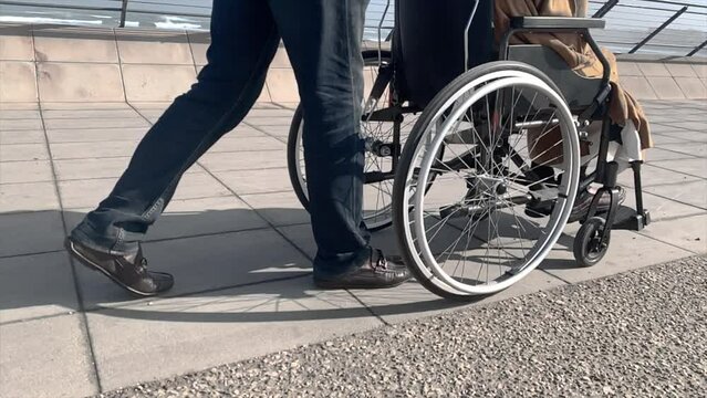 Closeup of old man with paraplegia riding wheelchair along seafront on sunny day. Strong male arms pushing wheels. Blurred seascape background. Side view. Disability, lifetsyle, motivation concept.