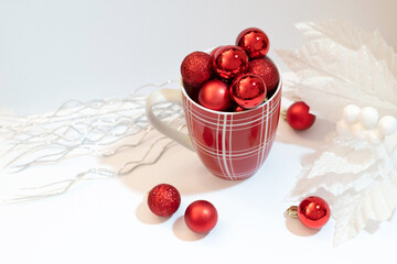 Red ornaments placed in a coffee mug against a snow-white background associated with holiday festivities symbolize aspects of the season, from festive joy to the spirit of giving