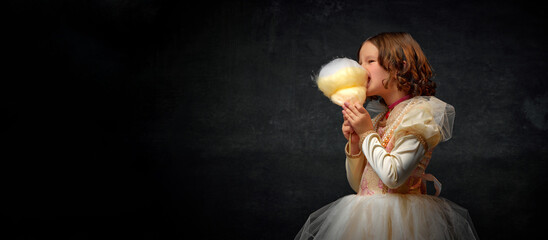 Banner. Little princess in eats greedily sweet cotton candy against dark vintage background....
