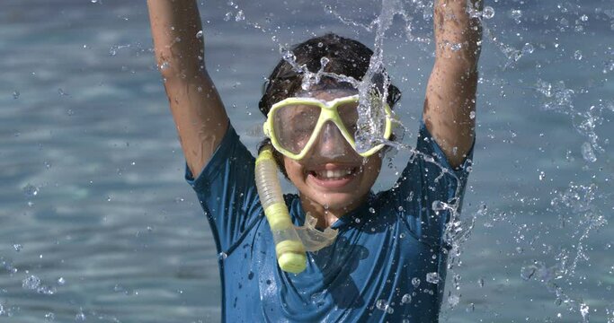 Super slow motion of happy smiling little girl wearing diving suit and snorkel mask while having fun at sea during summer holidays family travel vacation.