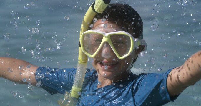 Super slow motion of happy smiling little girl wearing diving suit and snorkel mask while having fun at sea during summer holidays family travel vacation.