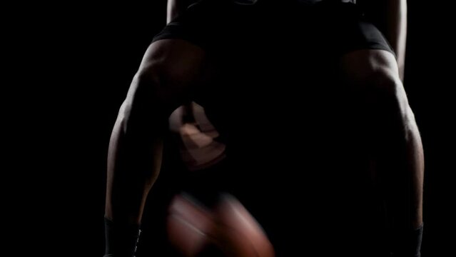 Basketball player bouncing a ball. African american sports man practicing against black background. Abstract body shot front view.