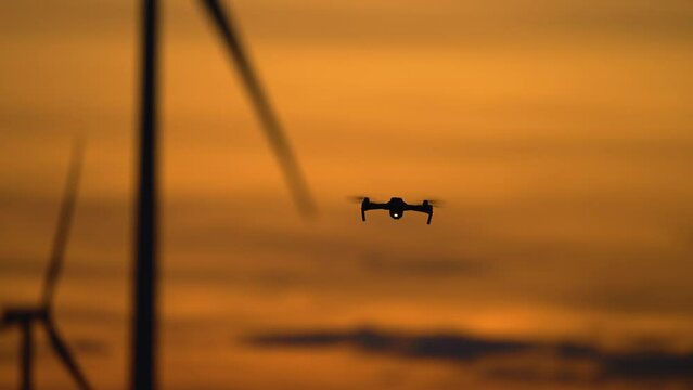 Inspecting Wind turbines produce energy using drone unmanned aircraft, quadrocopter uses for study advantages and drawbacks of electric station at amazing cloudy colorful sunset. Generating renewable