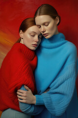 Portrait of two women embracing in red and blue sweaters, abstract warm background - obrazy, fototapety, plakaty