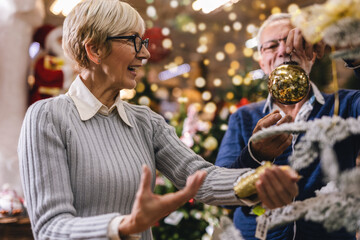 Senior couple at Christmas Market buying decor toys and balls. Concept of Christmas and New Year shopping.