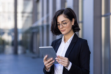 Close-up photo of serious young businesswoman talking on the street near work office on video call on tablet, watching and developing project, startup, waiting for meeting