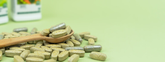 Natural vitamins and supplements in a wooden spoon on a green background. Banner. Close-up. Copy space. Selective focus.