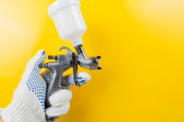 Manual and paint spray gun at work on a yellow background - obrazy, fototapety, plakaty