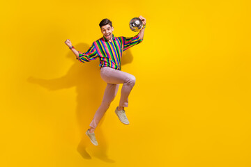 Fototapeta na wymiar Full body photo of young man brunet hair club man loves nightlife holding shiny disco ball when jumping isolated on yellow color background