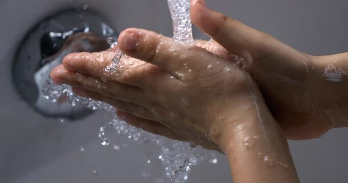 Super slow motion close up of little girl is pouring clean fresh transparent water in her hands from bathroom tap while washing it.