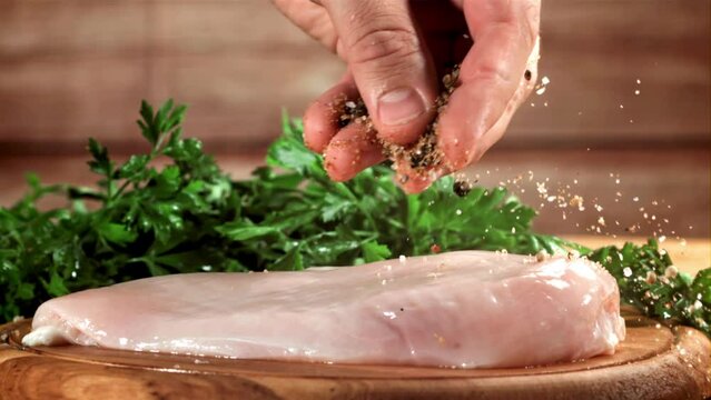 A hand sprinkles spices and salt on raw chicken fillet. Filmed on a high-speed camera at 1000 fps. High quality FullHD footage