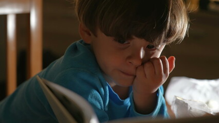 One small boy absorbed by story book at night before bed. Close-up child staring at book, flipping...