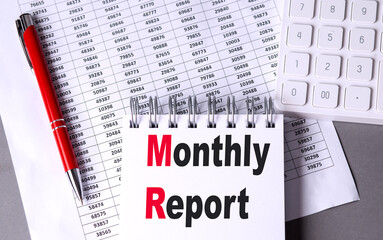 MONTHLY REPORT text on notebook with pen, calculator and chart on grey background