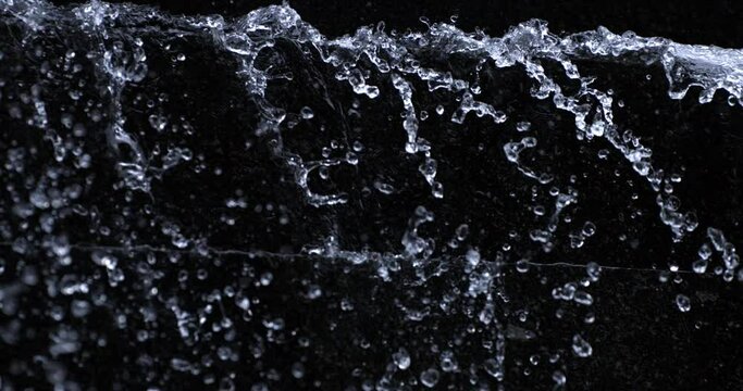 Super slow motion macro of water cascade with flowing drops texture on dark brick background. Filmed on high speed cinema camera at 1000 fps.