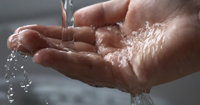 Super slow motion macro of young woman is pouring clean fresh transparent water in her hand from bathroom tap while washing it.