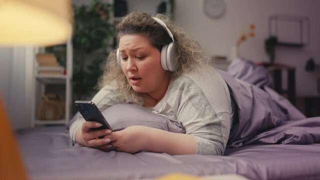 Happy overweight female listening music on smartphone, wearing earphones, relax
