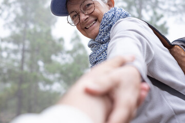 Portrait of happy senior woman walking in pine forest giving hand to someone else to rise