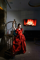 Pretty woman in a luxurious red dress posing in a luggage trolley.Fashion shooting concept