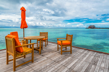 Scenic view of wooden furniture on terrace in Maldives with turquoise water and dramatic sky