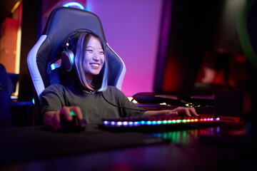 Portrait of smiling Asian woman enjoying video games in cybersports club with neon lights, copy...