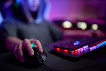 Close up of female hand holding computer mouse in cybersports club with neon lights, copy space