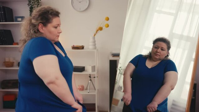 Unhappy plus size woman wearing small blouse, upset with mirror reflection