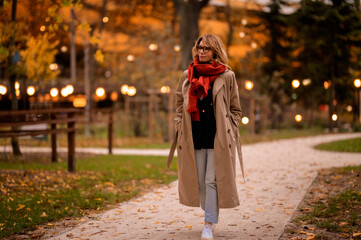 Full length of a mid aged woman wearing trench coat at scarf at the park autumn
