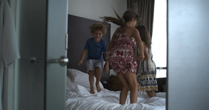 Super slow motion of carefree kids are having fun to jump on bed together in complete freedom and happiness in hotel room during holidays family vacation trip.