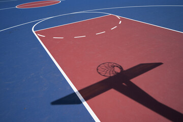 Empty blue outdoor basketball court with the net and backboard in shadow