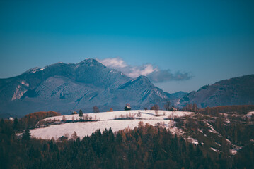 Winter landscape with snow-covered hills and mountains background. Human settlements in wild areas....