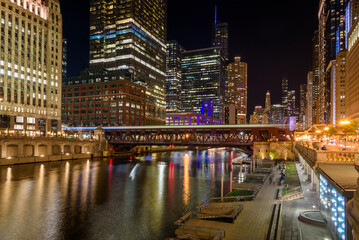 Nigh view of Chicago downtow and river. Light trail left by a passing train are visible on the bridge in foreground.