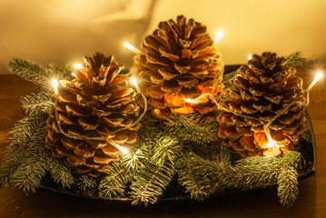 Holiday decoration with cones on fir branches and fairy lights on a wooden table. Selective focus.