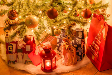 Close upof wrapped gifts and a lantern under an indoor Christmas tree. Selective focus.