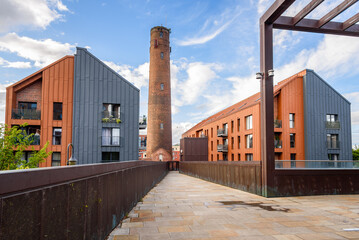 Deserted footbridge leading to two modern apartment buildings overlooked by a old brick tower on a sunny summer day