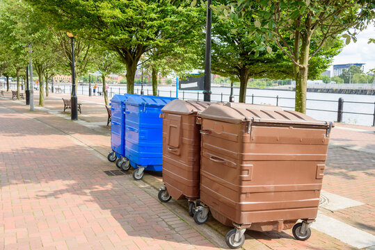 Large recycling bins along a tree lined harbourside footpath on a sunny summer day