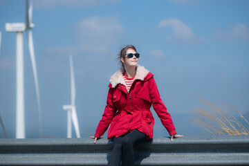Obraz premium On the background of windmills, A young woman in a red jacket is enjoying her winter vacation.