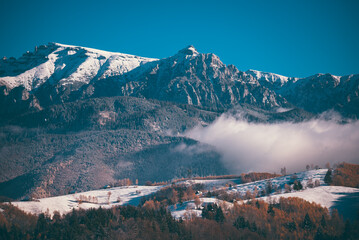 Winter landscape with snow-covered hills and mountains background. Human settlements in wild areas....