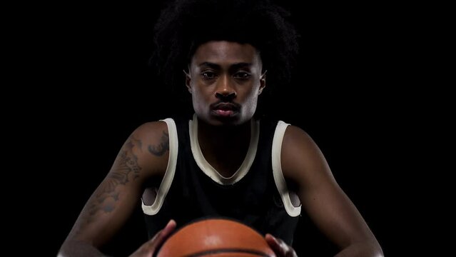 Basketball player sitting on a bench holding a ball. Concentrated african american sports man against black background