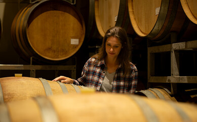 Portrait of a young woman surrounded by wine barrels In her winery