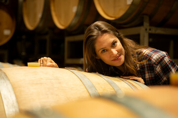 Portrait of a young woman surrounded by wine barrels In her winery - obrazy, fototapety, plakaty
