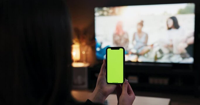 Freelance concept young woman holding cell phone smartphone with green screen mockup in hands scrolling swiping surfing internet observing imaged photos chatting with friends while watching tv.