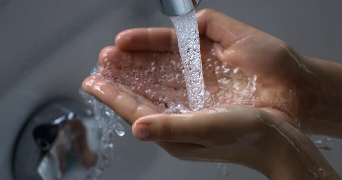 Super slow motion close up of little girl is pouring clean fresh transparent water in her hands from bathroom tap while washing it.