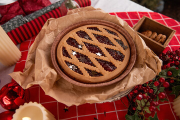 Top view of Christmas table with open cranberry pie on red tablecloth with candles, advent wreath