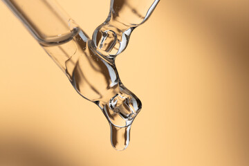 Two glass pipettes with transparent makeup gel, close-up on a beige background. Close-up of a liquid skin care product.