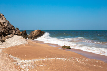 Fototapeta na wymiar Sea sandy shore and sea with waves hitting the rocks. Seascape